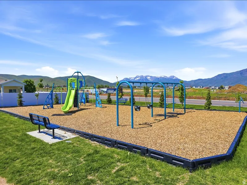 Community playground featuring a slide, swings, and benches within a wood chip surface