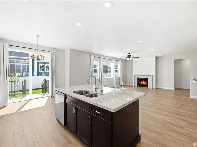 Open-concept living area featuring light wood-finish flooring, a kitchen island with a double basin sink and light-toned countertop, and a fireplace with a white mantel