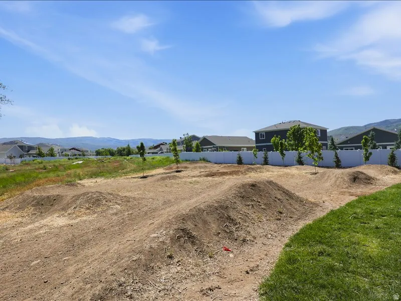 Dirt terrain with sculpted mounds, bordered by a white privacy fence and partial green lawn