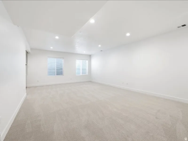 Expansive room featuring plush light-toned carpeting, recessed lighting, and crisp white walls
