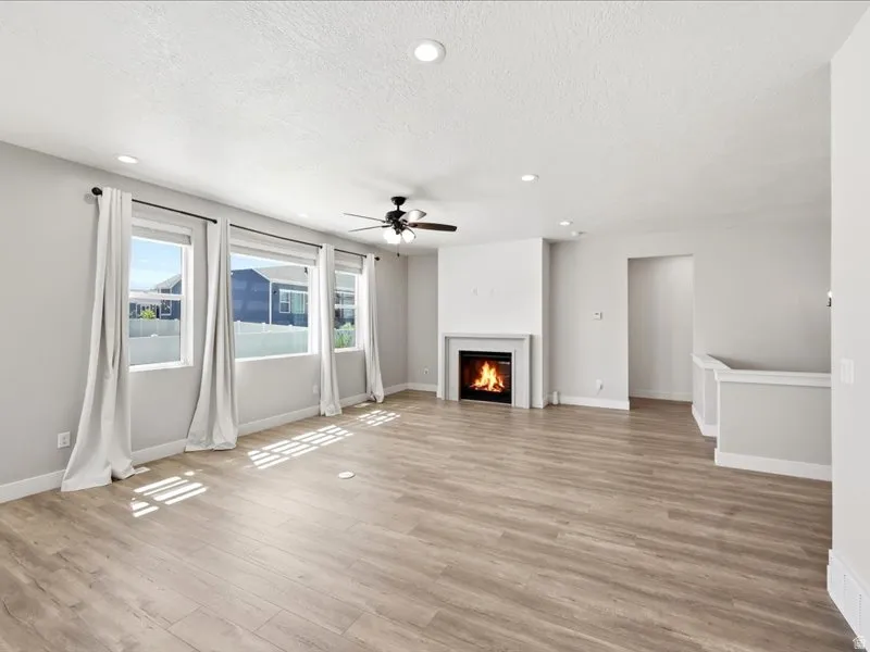 Living space featuring wood-finish flooring, a fireplace with a white mantel, recessed lighting, and a ceiling fan