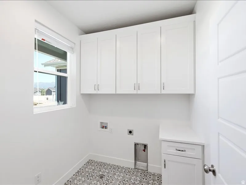 Dedicated laundry space featuring white cabinetry with brushed nickel hardware, a single window, patterned floor tile, and a built-in counter with additional storage