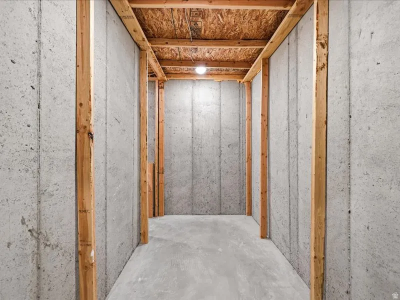 Unfinished concrete basement area with exposed wood framing, concrete floor, and overhead lighting