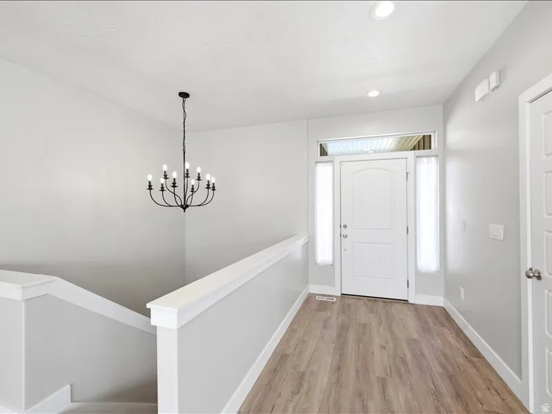 Entryway featuring wood-finish flooring, a white paneled entry door with sidelights and transom window, a black wrought iron chandelier, recessed lighting, and a painted staircase with white trim