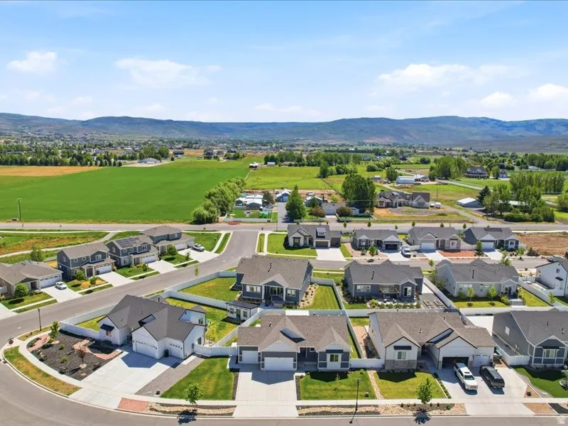 Aerial perspective showcasing a residential community with contemporary homes, mountain backdrop, and expansive green fields