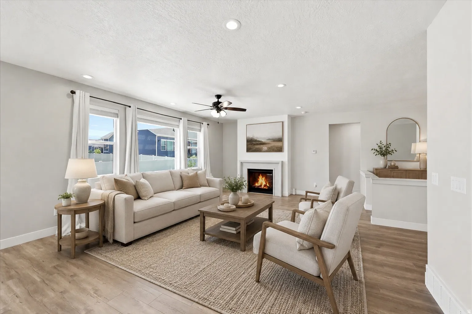 Living space featuring wood-finish flooring, a white mantel fireplace, three large windows, a ceiling fan with light fixture, and recessed lighting