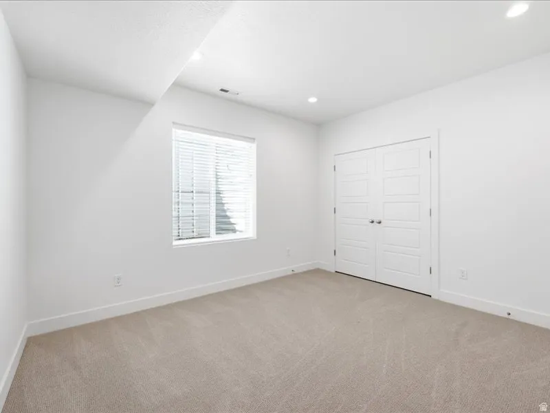 Carpeted room featuring a double-pane window with blinds, white walls, recessed lighting, and a double-door closet with paneling