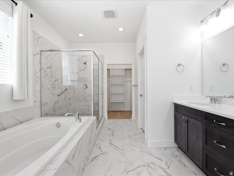 Bathroom featuring a built-in tub, a glass-enclosed shower with a grab bar, a single vanity with a white countertop and dark cabinetry, and white tile flooring with gray veining