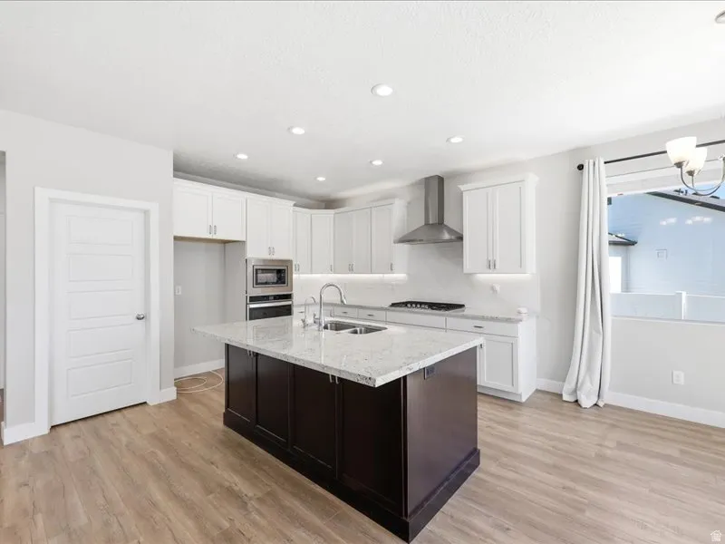 Kitchen featuring a dark-toned island with a light-toned countertop, white cabinetry, stainless steel range hood, built-in stainless steel oven and microwave, and wood-finish flooring