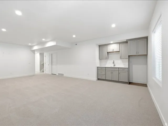 Spacious carpeted room featuring a wet bar with gray cabinetry, white subway tile backsplash, and a stainless steel faucet