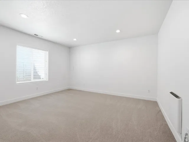 Spacious room featuring neutral carpeting, white walls, and a large window with horizontal blinds