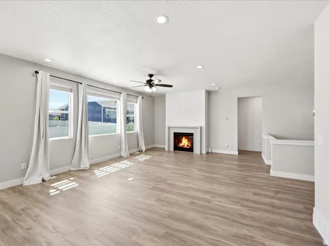 Living space featuring wood-finish flooring, a fireplace with a white mantel, recessed lighting, and a ceiling fan