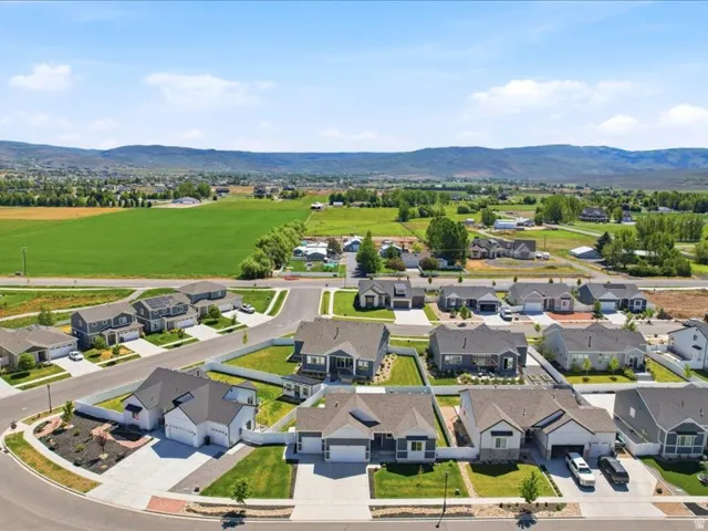 Aerial perspective showcasing a residential community with contemporary homes, mountain backdrop, and expansive green fields