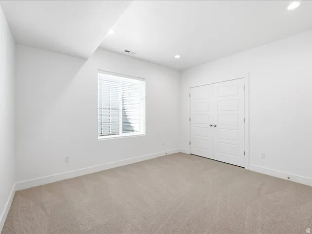 Carpeted room featuring a double-pane window with blinds, white walls, recessed lighting, and a double-door closet with paneling