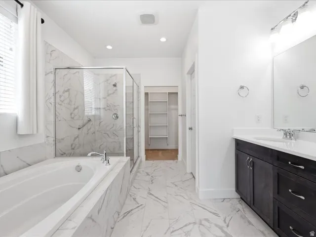 Bathroom featuring a built-in tub, a glass-enclosed shower with a grab bar, a single vanity with a white countertop and dark cabinetry, and white tile flooring with gray veining