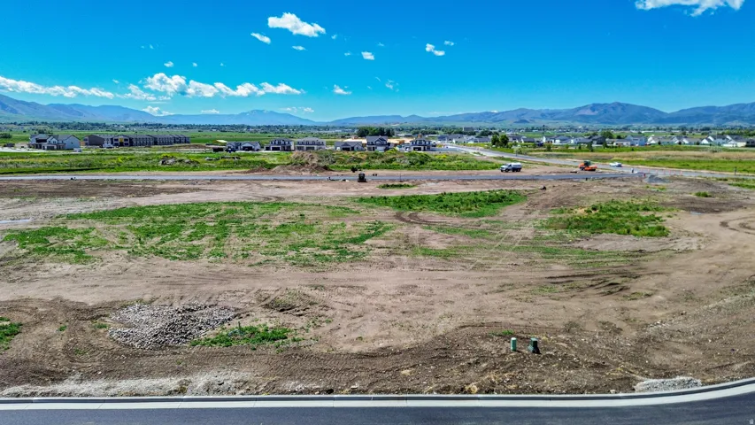 Expansive land parcel featuring prepared ground, with scattered green growth and visible utility markers