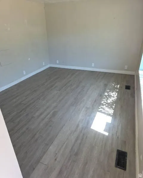 Spacious room featuring wood-finish flooring, light-toned walls, and white baseboards