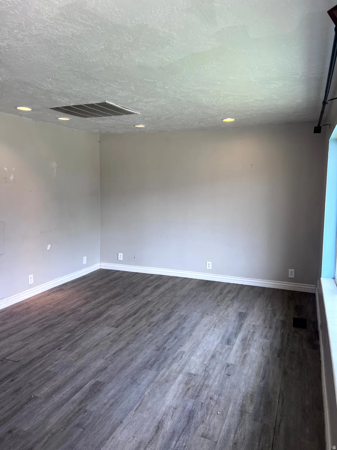 Spacious room featuring wood-finish flooring, light grey walls, white baseboards, and recessed ceiling lighting