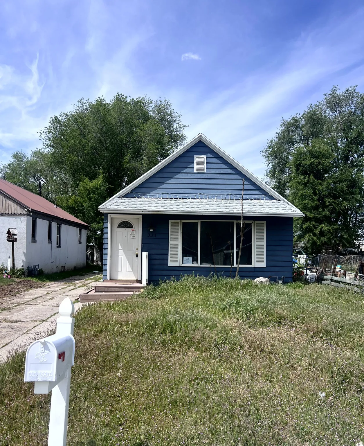 Blue horizontal siding, white gable trim, white front door with arched window, large front window with white shutters, and a white shingle roof