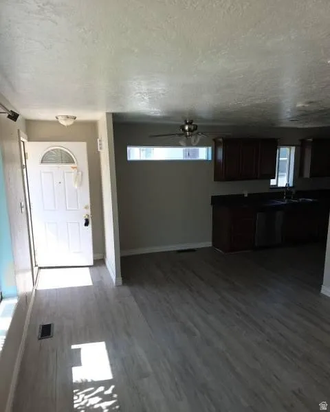 Open-concept living space with wood-finish flooring, a contemporary ceiling fan, and a transom window providing natural light