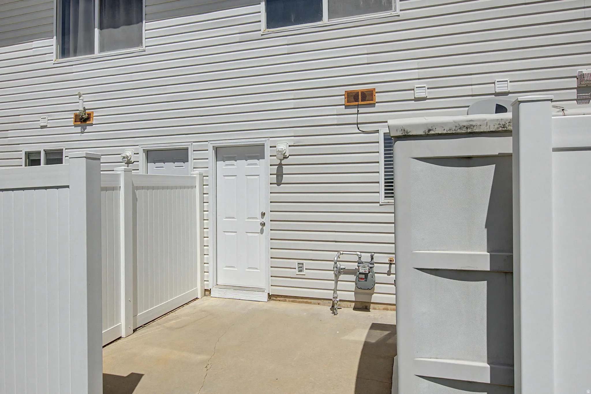 Rear exterior featuring white vinyl siding, a private concrete patio, and a white paneled privacy fence