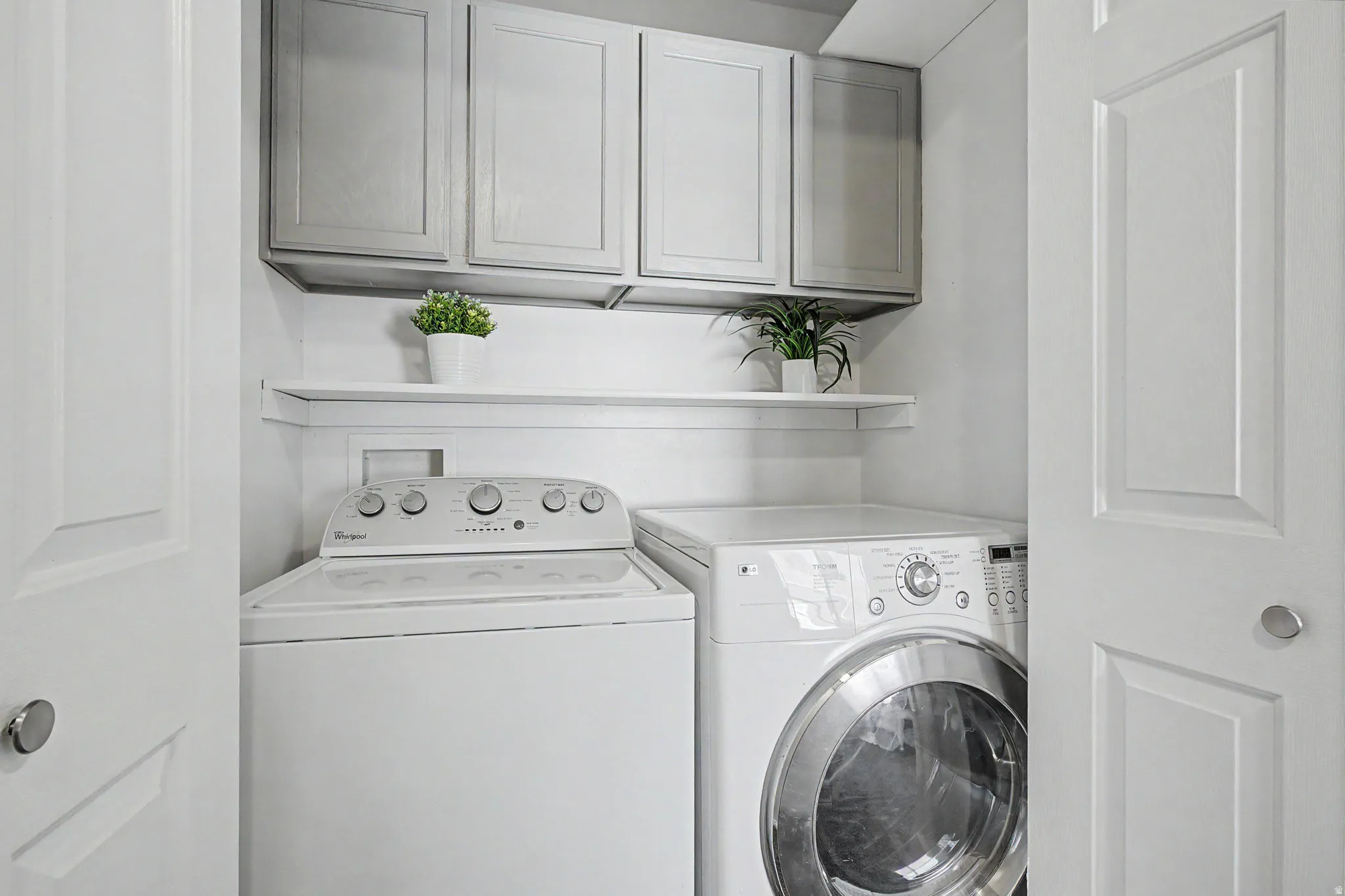 Dedicated laundry closet featuring a top-load washer, front-load dryer, and upper cabinetry with integrated shelving