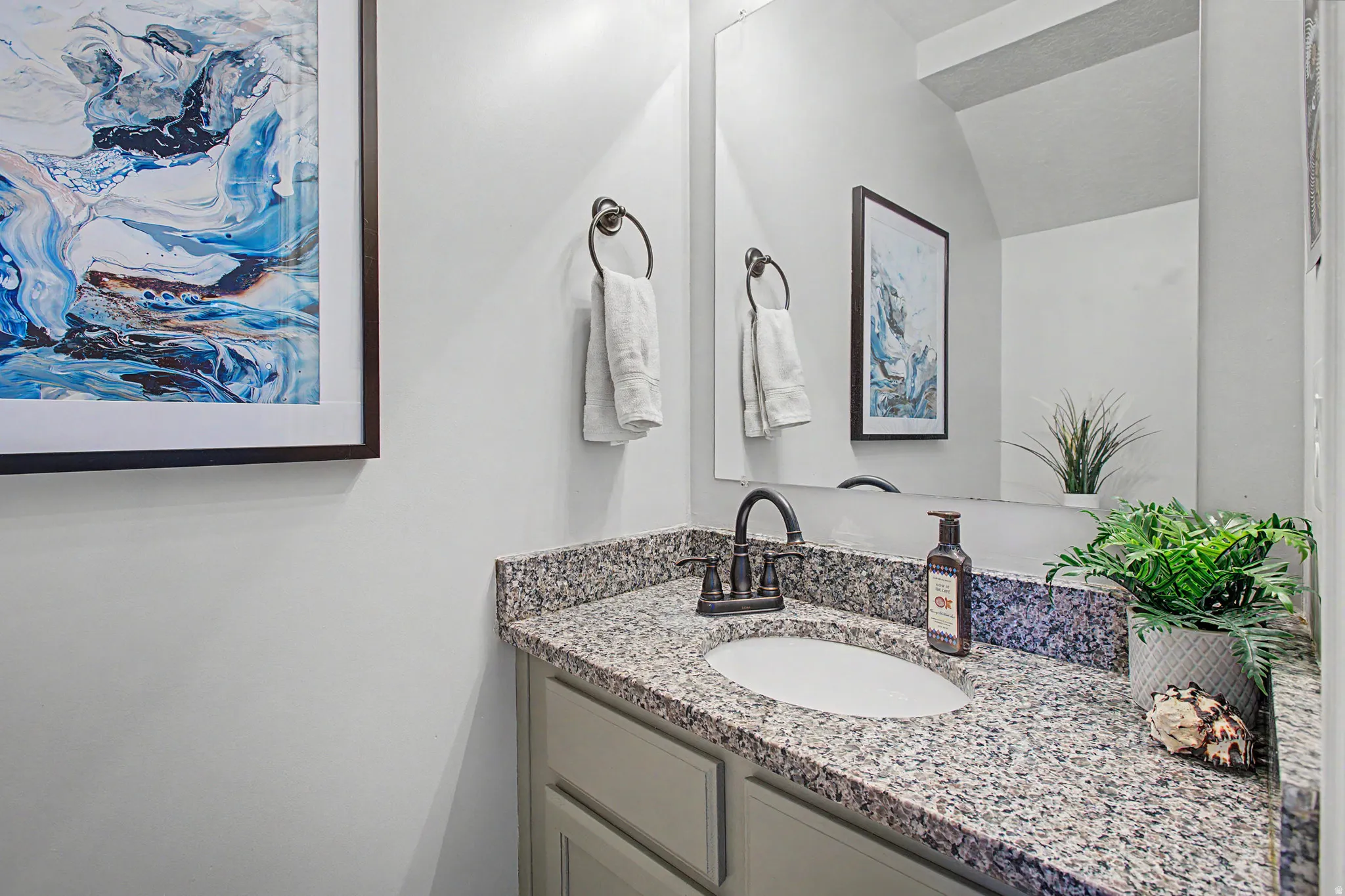 Vanity featuring a stone countertop, an undermount sink, a dark bronze faucet, and a large wall mirror