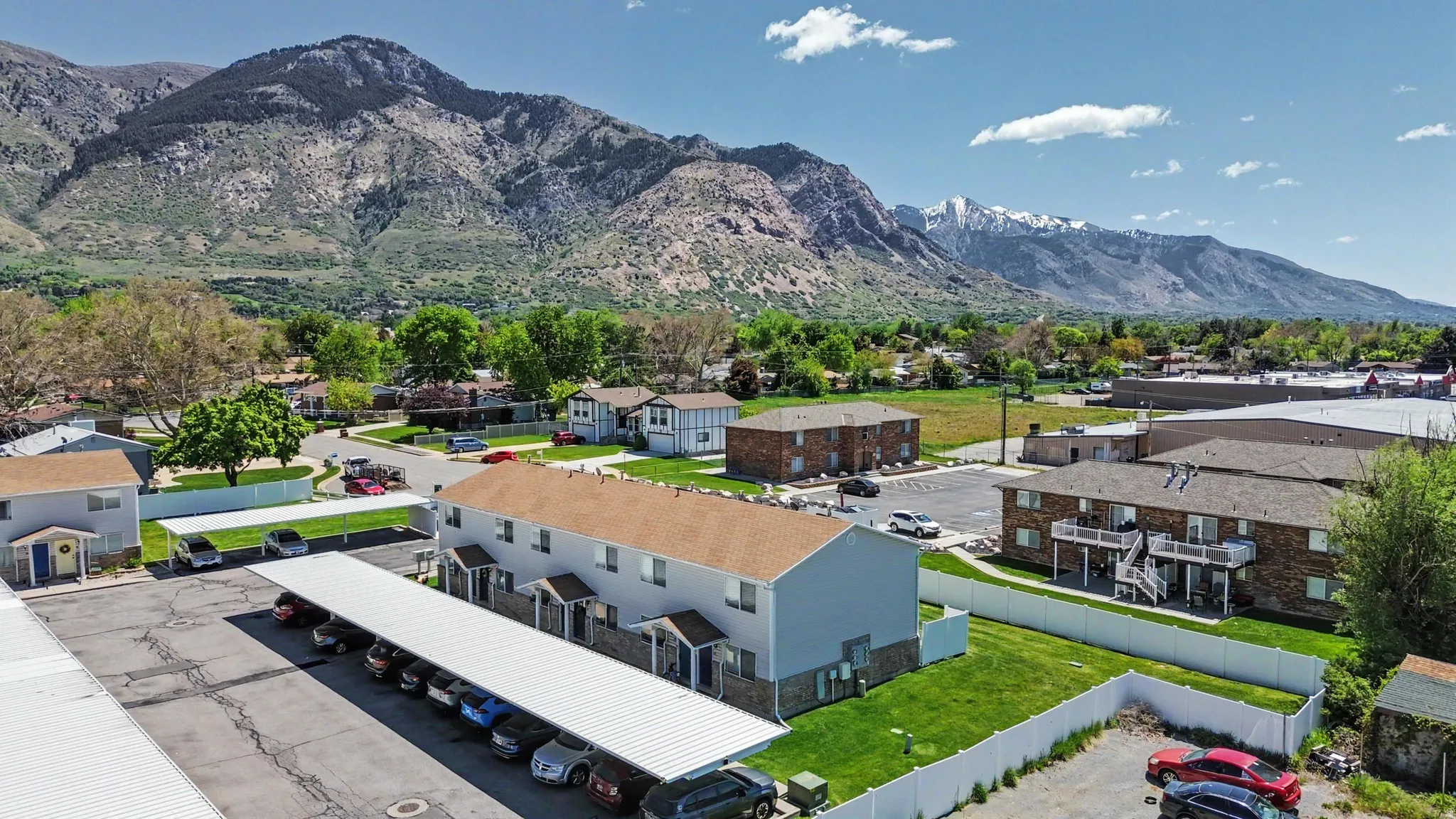 Expansive property featuring multiple residential buildings with tan shingle roofs, covered parking structures, and green lawns