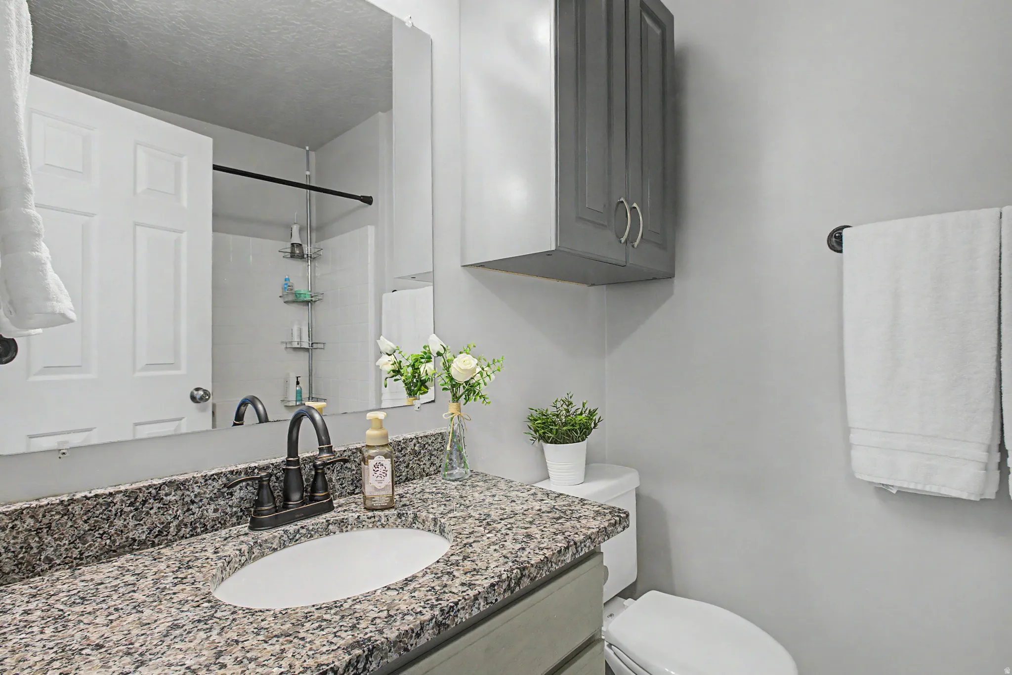 Bathroom vanity featuring a granite countertop with an oval under-mount sink and a bronze-finish faucet