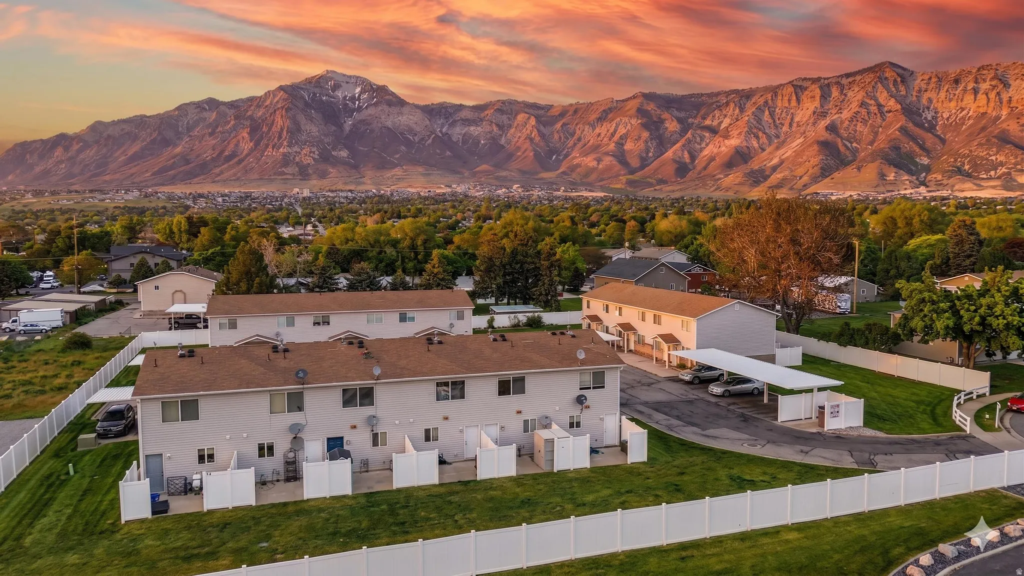 Multiple townhome-style buildings with brown shingle roofs, white privacy fencing, and paved parking areas