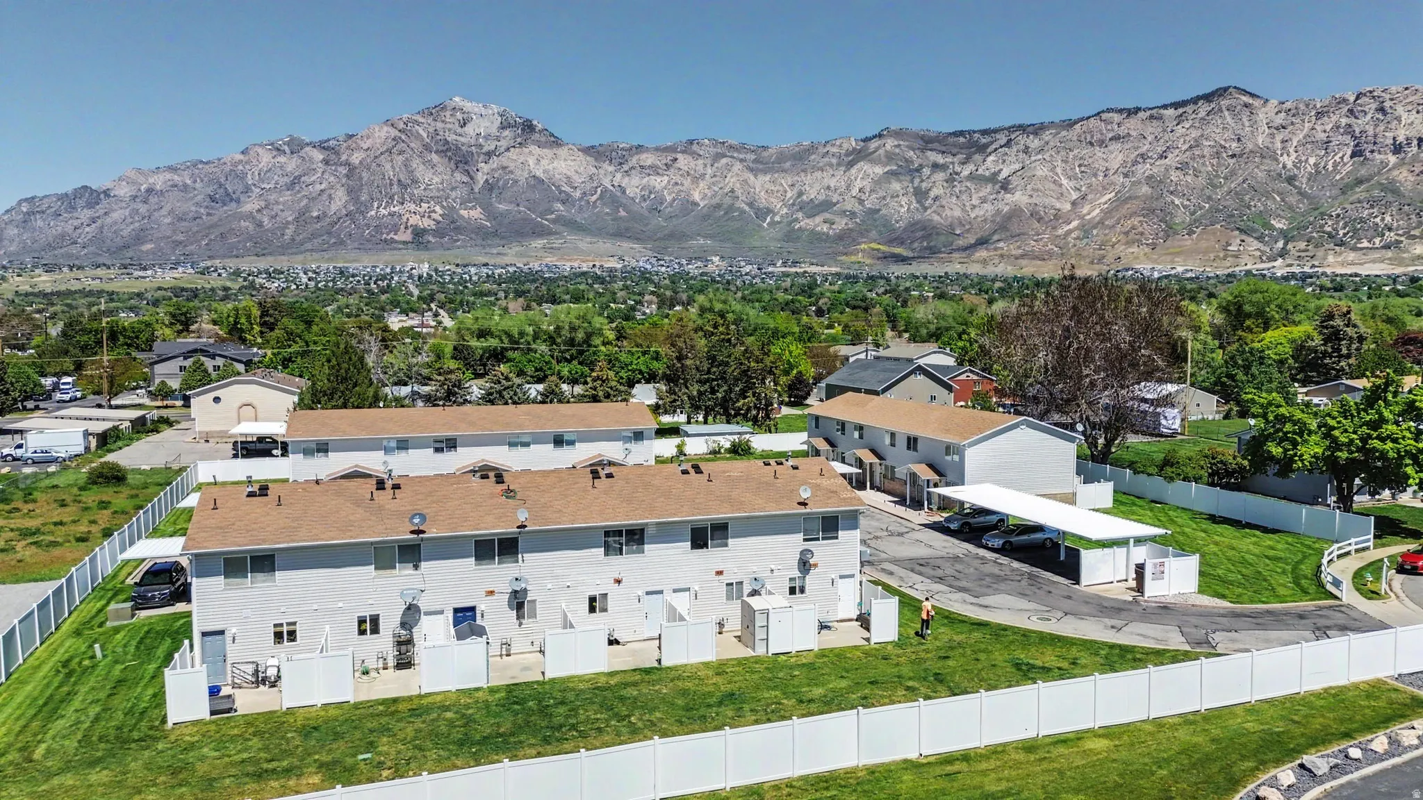 Multi-unit property featuring light-colored siding, brown shingle roofs, and individual private patio areas