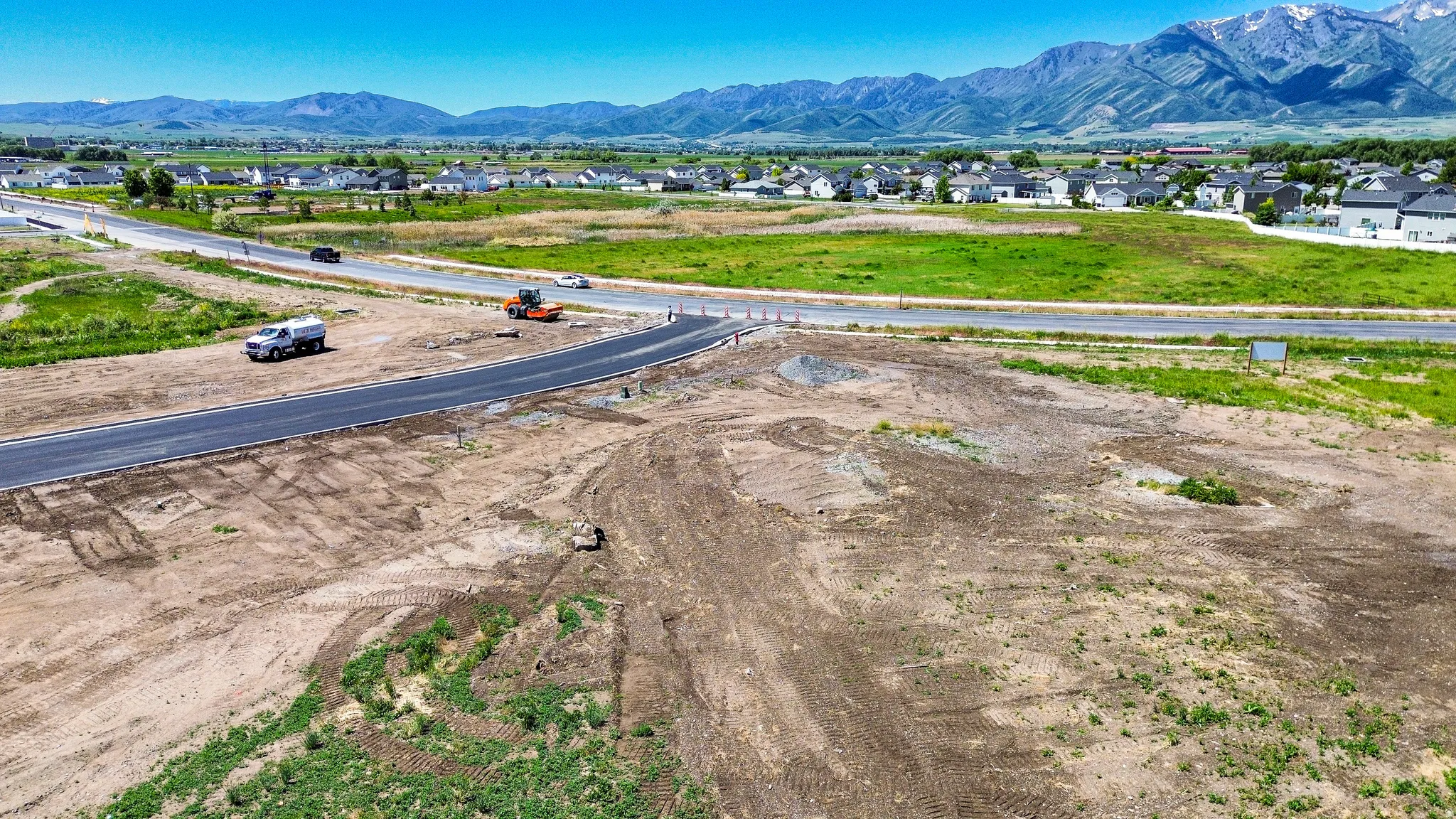 Expansive undeveloped land featuring a newly paved roadway and distant mountain range backdrop