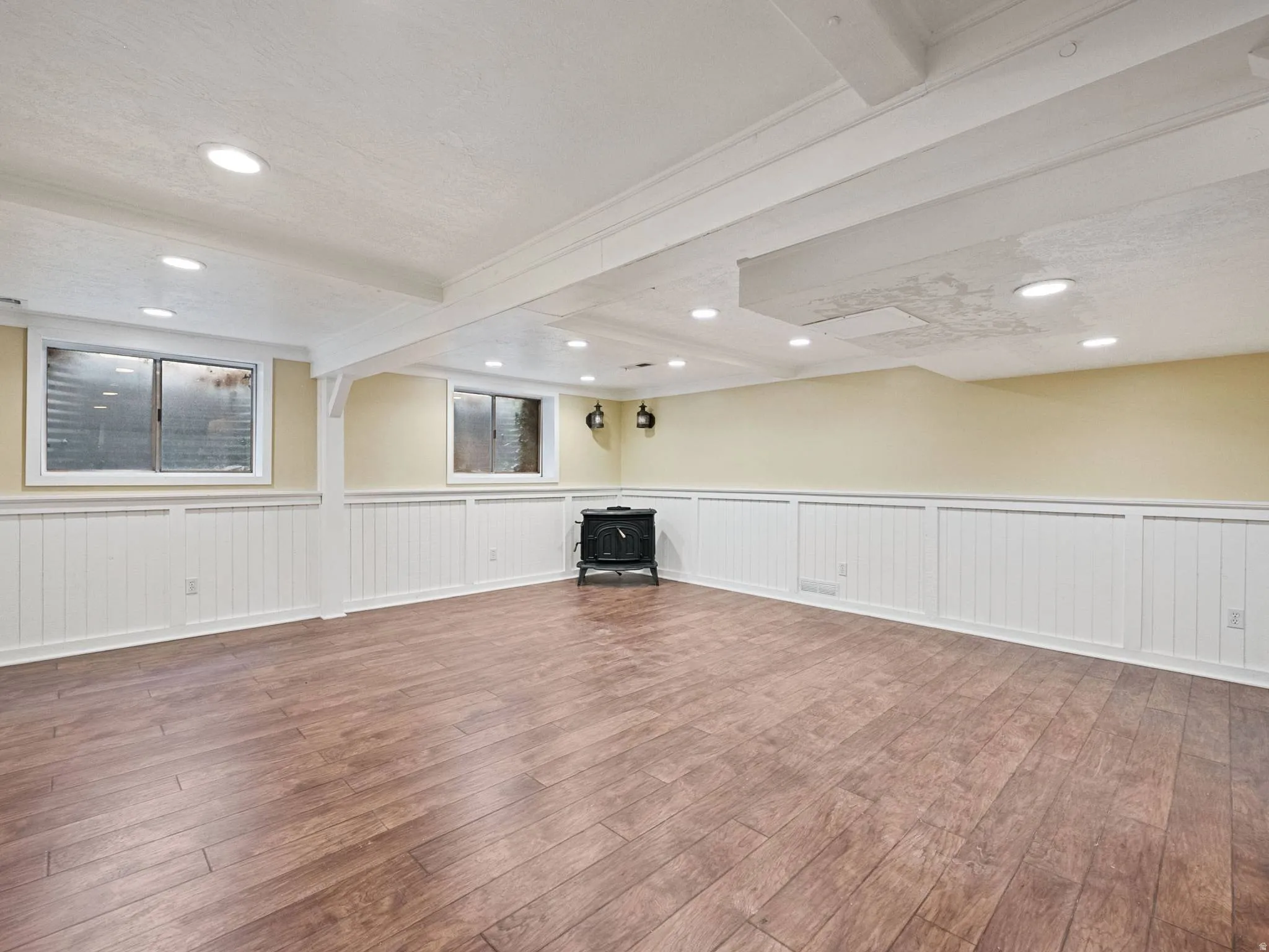 Spacious basement recreation or family room finished room featuring wood-finish flooring, white wainscoting, and recessed lighting