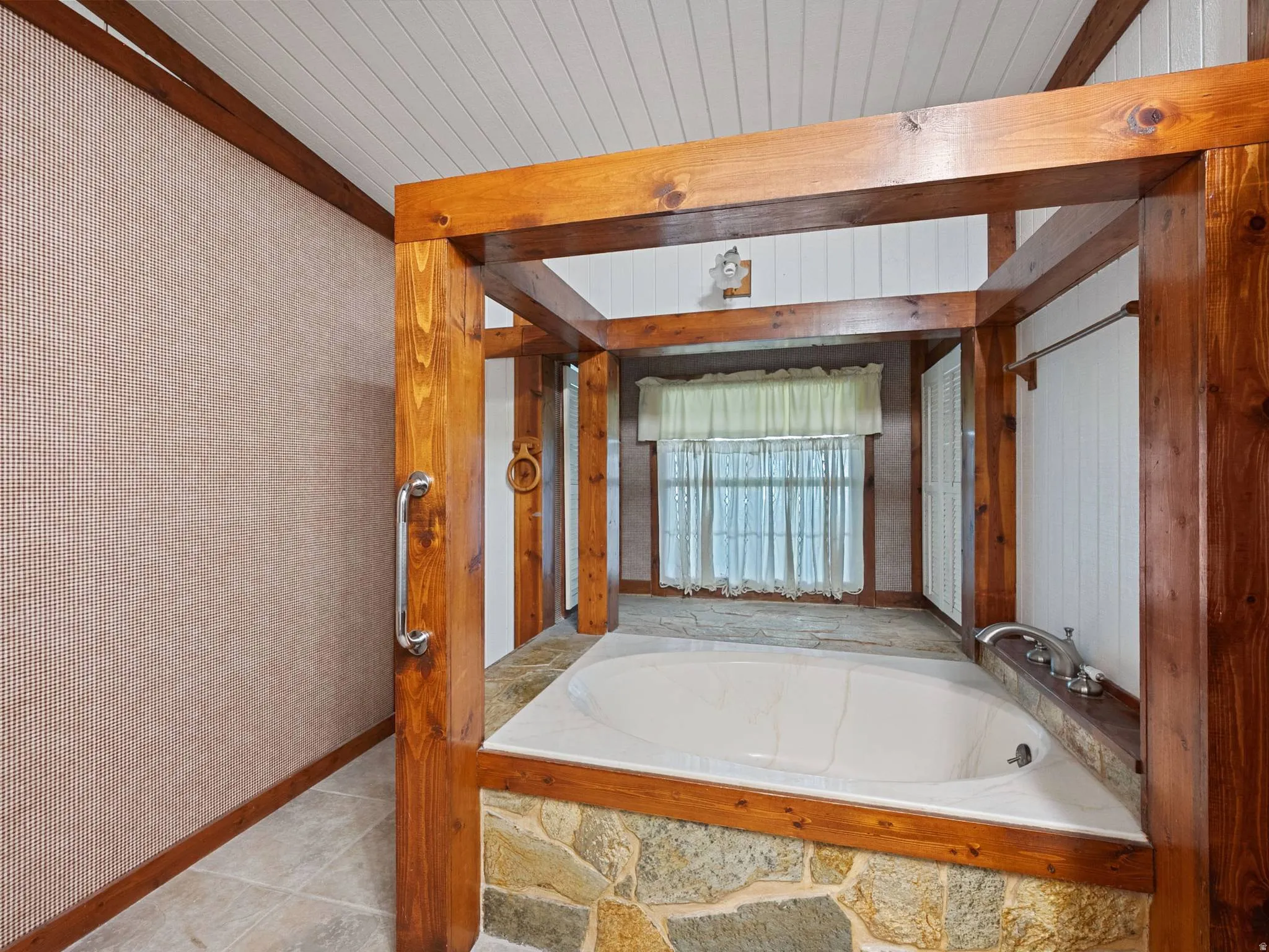 Master bathroom showing a soaking tub with stone surround, wood-finish beam structure, and panel ceiling