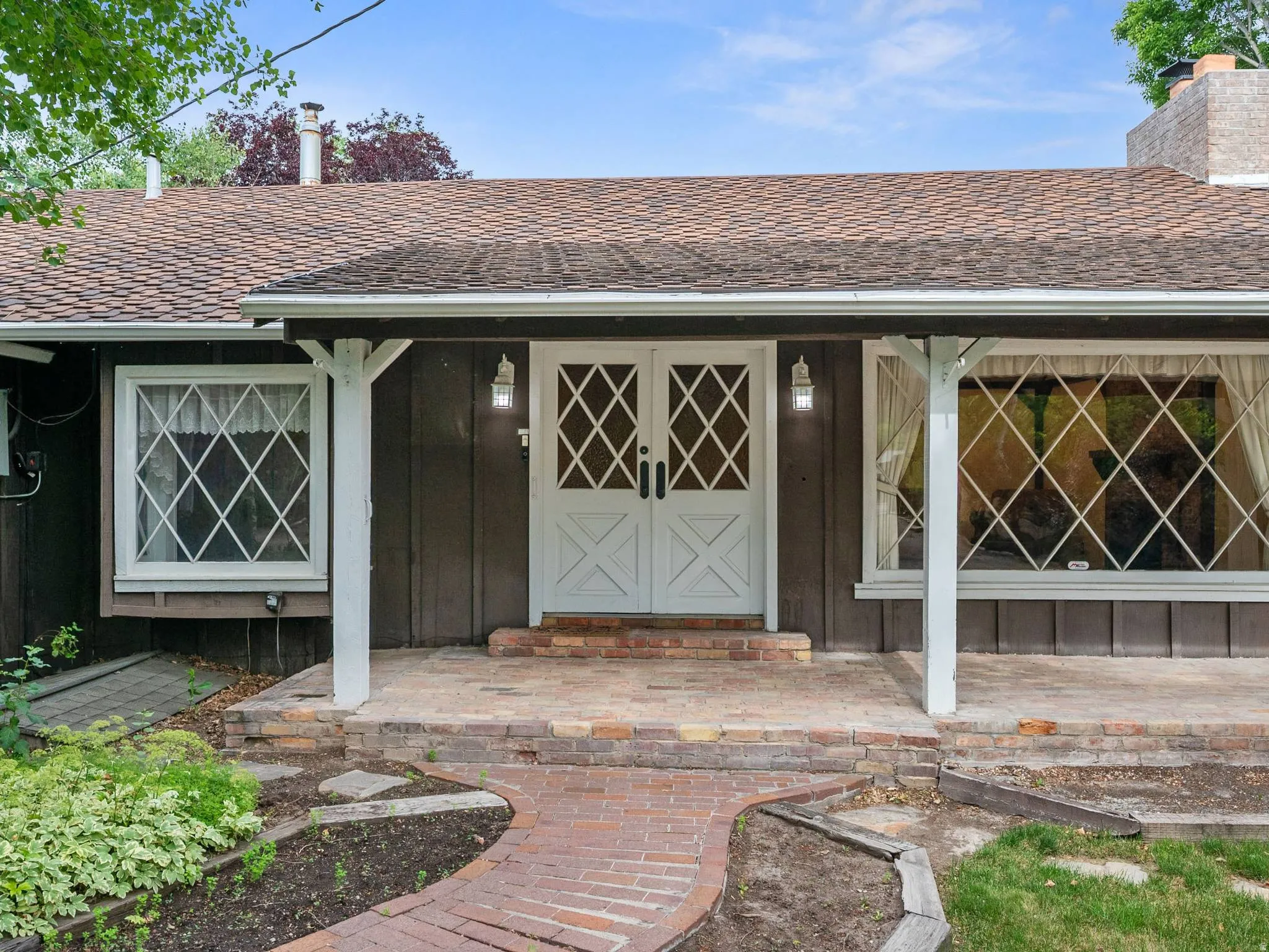 Front entry featuring double doors with diamond-pane windows, a covered porch with white posts, and brick detailing