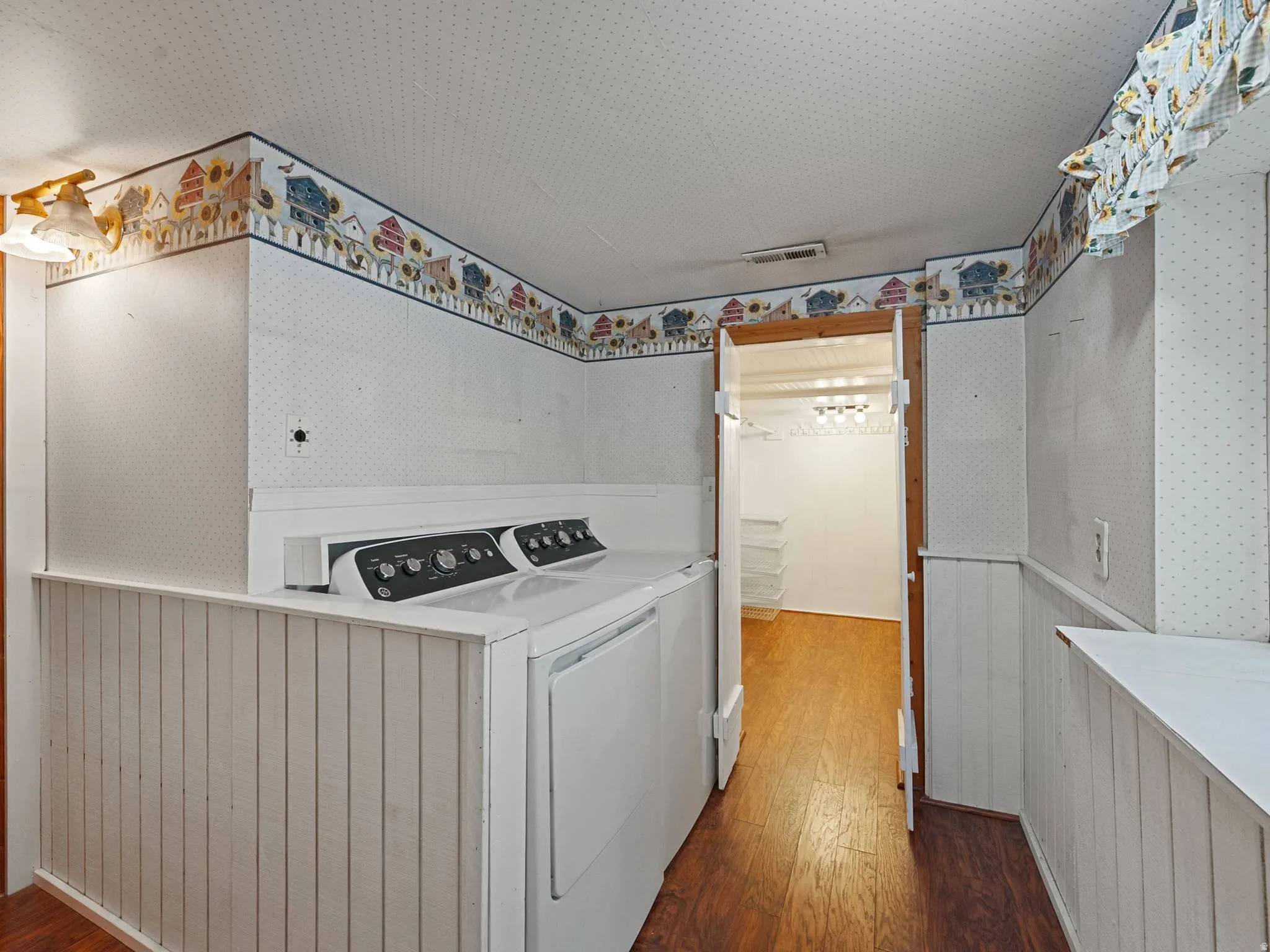Dedicated laundry area with wood-finish flooring, white paneled wainscoting, and an adjacent walk-in storage closet