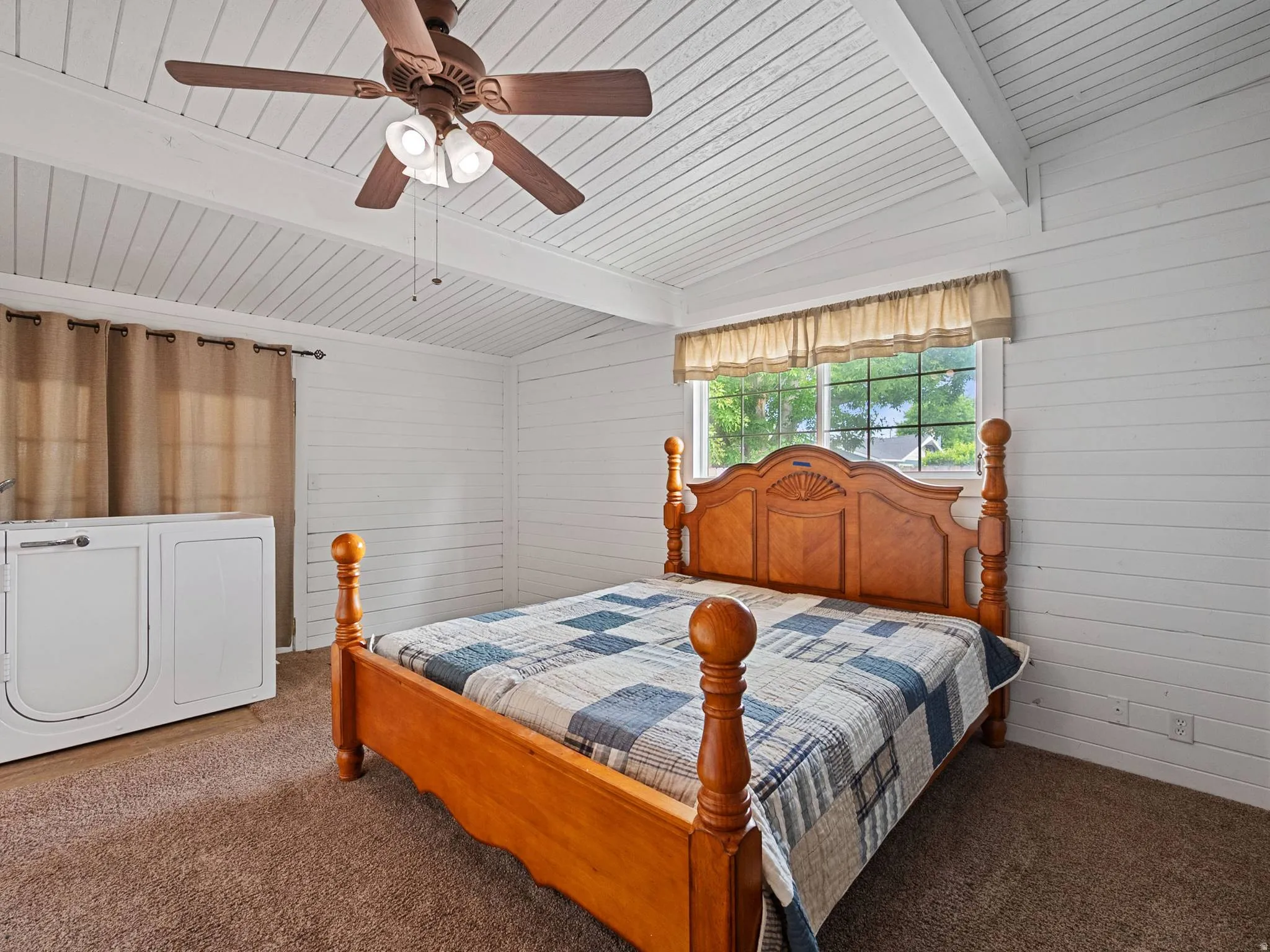 Spacious master bedroom featuring white shiplap walls, a vaulted plank ceiling with exposed beams, and a ceiling fan with integrated lighting. There are French doors behind the walk-in tub which is being removed from the home.