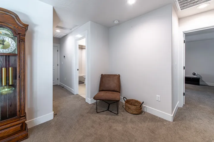 Carpeted hallway with white baseboards, recessed lighting, and a visible doorway to a bathroom with a white toilet and light-colored flooring