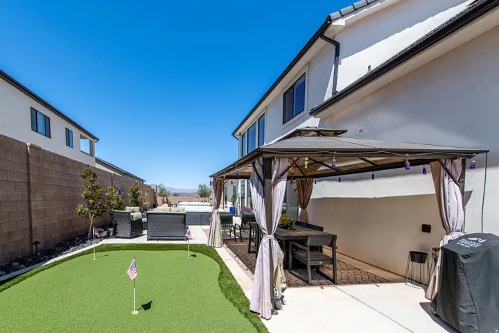 Outdoor living area featuring a covered patio, artificial turf putting green, and a hot tub