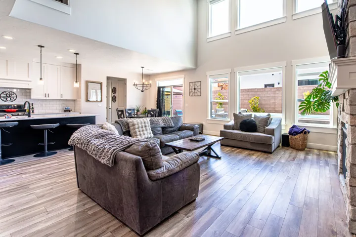 Open concept living area featuring wood-finish flooring, a stone-faced fireplace with a mantel, and high ceilings with upper transom windows