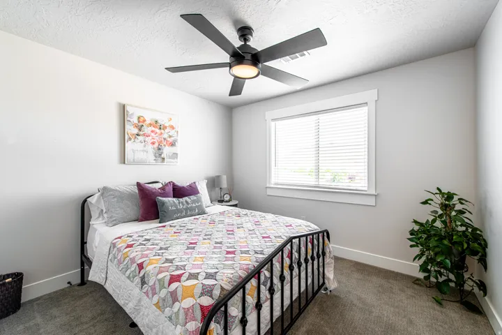 Bedroom featuring a large window with white blinds, a contemporary ceiling fan with integrated lighting, and neutral-toned carpeting