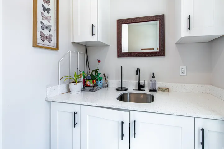 White shaker cabinetry with matte black hardware, speckled countertop, undermount stainless steel sink with a matte black faucet, and a framed mirror
