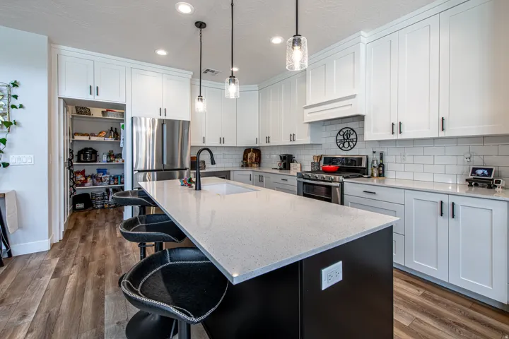 Modern kitchen featuring a large center island with a light-toned countertop, white shaker-style cabinetry, and wood-finish flooring