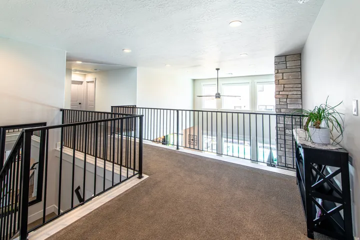 Carpeted loft area featuring black metal railing, a stone-clad pillar, and recessed lighting