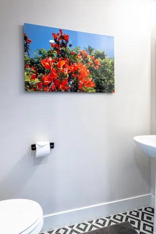 Pedestal sink and toilet with patterned floor tile, white baseboards, and a wall-mounted art piece