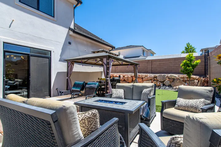 Private patio featuring a built-in fire pit, covered gazebo, artificial turf putting green, retaining wall with rock landscaping, and sliding glass door access to the interior