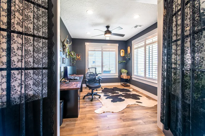 Office space featuring wood-finish flooring, dark accent walls, and white plantation shutters on multiple windows