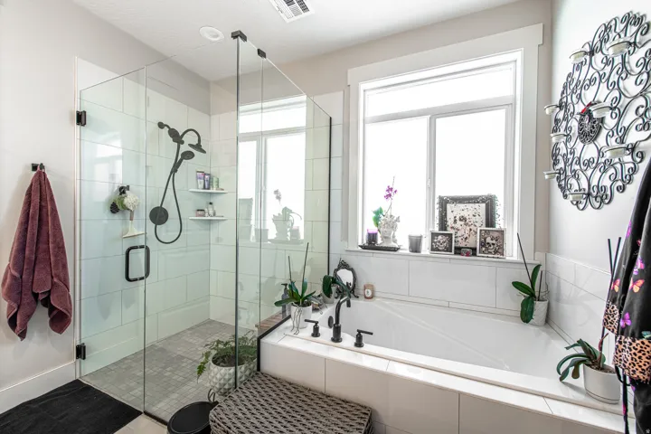 Spacious bathroom featuring a glass-enclosed shower with a matte black shower system, a separate soaking tub with matte black fixtures, a window above the tub, and white tile surrounds