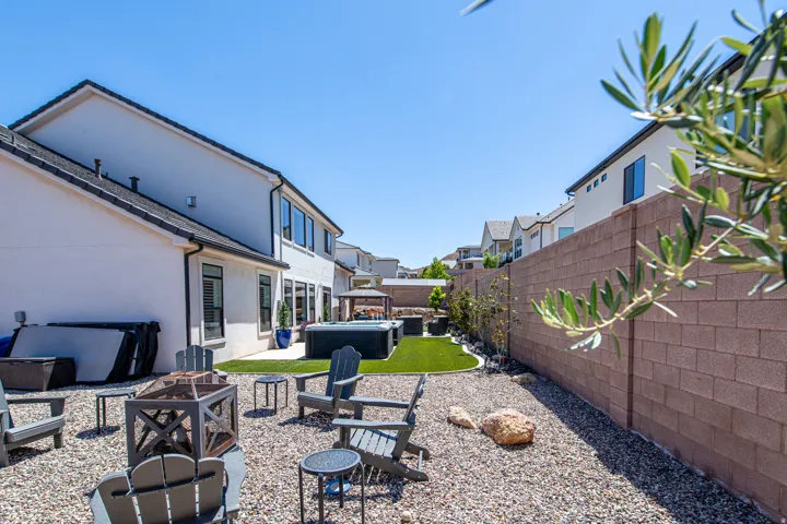 Expansive backyard featuring a gravel fire pit area, an artificial turf lawn, and a large spa