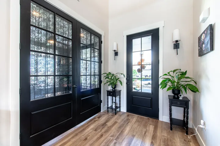 Wood-finish flooring throughout the entry, featuring a dark-paneled front door with glass inserts and two dark-paneled French doors